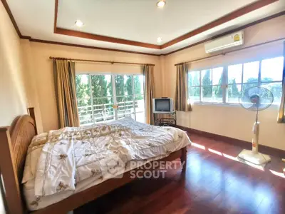 Spacious bedroom with large windows and balcony access, featuring wooden flooring and modern decor.