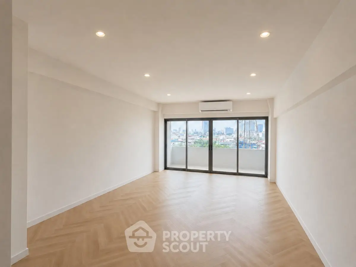Spacious modern living room with large windows and city view, featuring elegant wooden flooring.