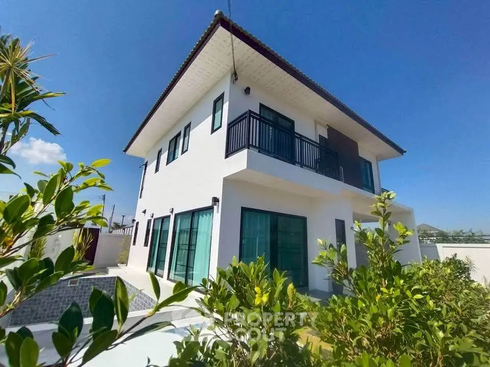 Stunning modern two-story house with lush garden and clear blue sky backdrop.