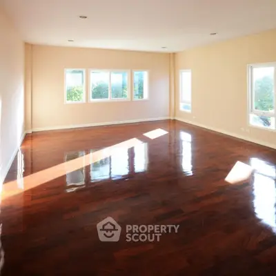 Spacious sunlit room with polished hardwood floors and large windows