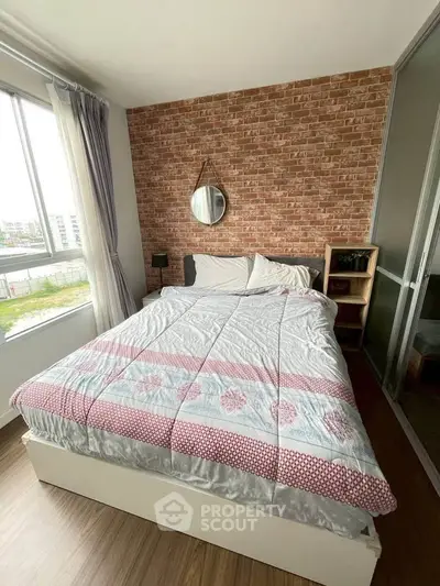 Cozy bedroom with brick accent wall and large window offering natural light and scenic view.
