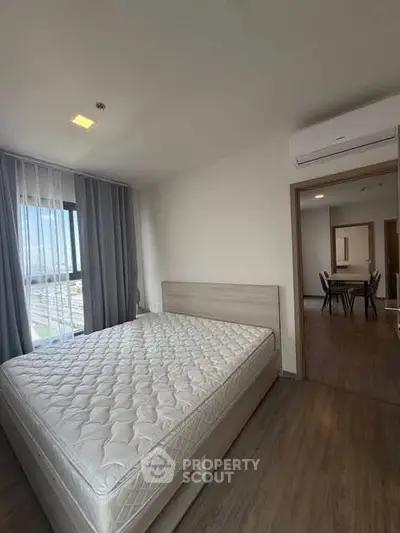 Modern bedroom with large window and dining area view, featuring sleek wooden flooring and neutral decor.