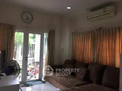 Cozy living room with brown sofa and air conditioning, featuring large windows and curtains.
