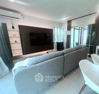 Modern living room with sleek design and large TV, featuring a cozy gray sofa and stylish decor.