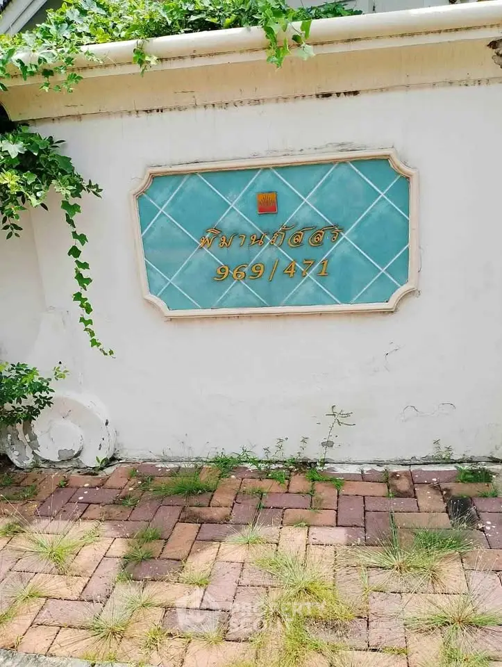 Charming property entrance with decorative wall sign and lush greenery.