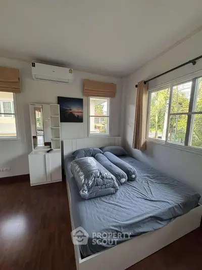 Cozy bedroom with large windows and air conditioning, featuring a modern bed and wooden flooring.
