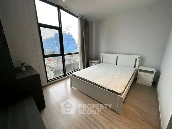 Modern bedroom with large window and city view, featuring sleek furniture and wooden flooring.