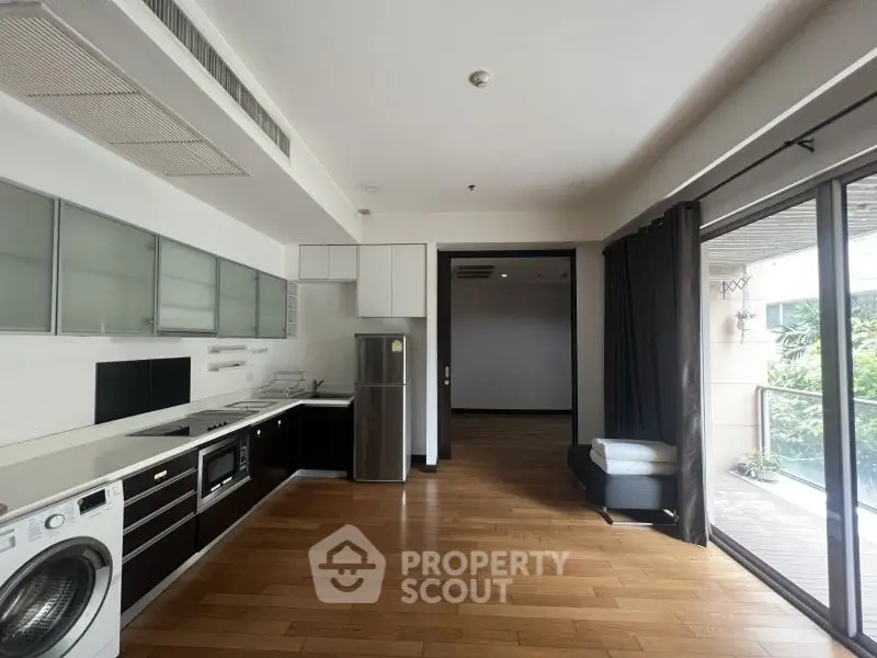 Modern kitchen with open layout and balcony access, featuring sleek appliances and hardwood floors.