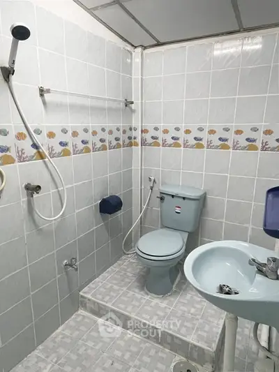 Compact bathroom with tiled walls, shower, and toilet in a cozy real estate property.