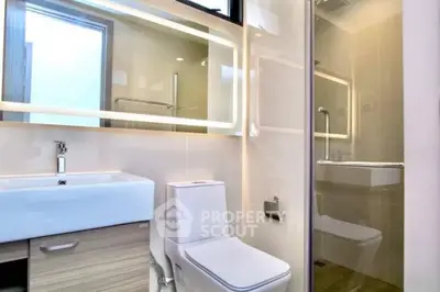 Modern bathroom with sleek design, featuring a large mirror, white fixtures, and a glass shower enclosure for a minimalist aesthetic.