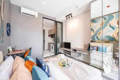 Modern bedroom with stylish decor and open view into kitchen area, featuring vibrant pillows and wall art.
