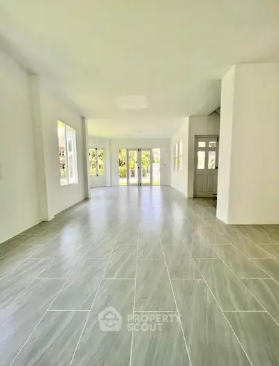 Spacious open-plan living room with large windows and tiled flooring, perfect for natural light and modern living.