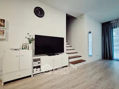 Modern living room with TV, white cabinet, and staircase in stylish home.