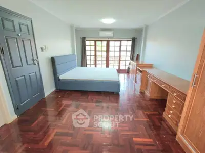 Spacious bedroom with wooden flooring and large windows for natural light.