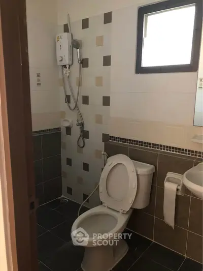 Compact bathroom with shower and toilet, featuring modern tile design and natural light from window.