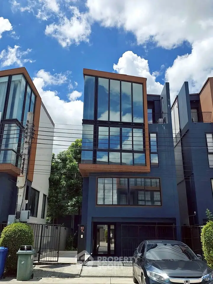 Modern multi-story townhouse with large glass windows and sleek design under a clear blue sky.