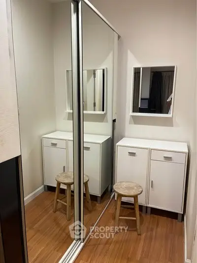 Modern bedroom with mirrored closet and wooden stool, showcasing sleek storage solutions.
