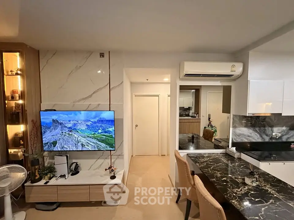 Modern living room with stylish decor and open kitchen layout, featuring a large TV and elegant marble countertop.