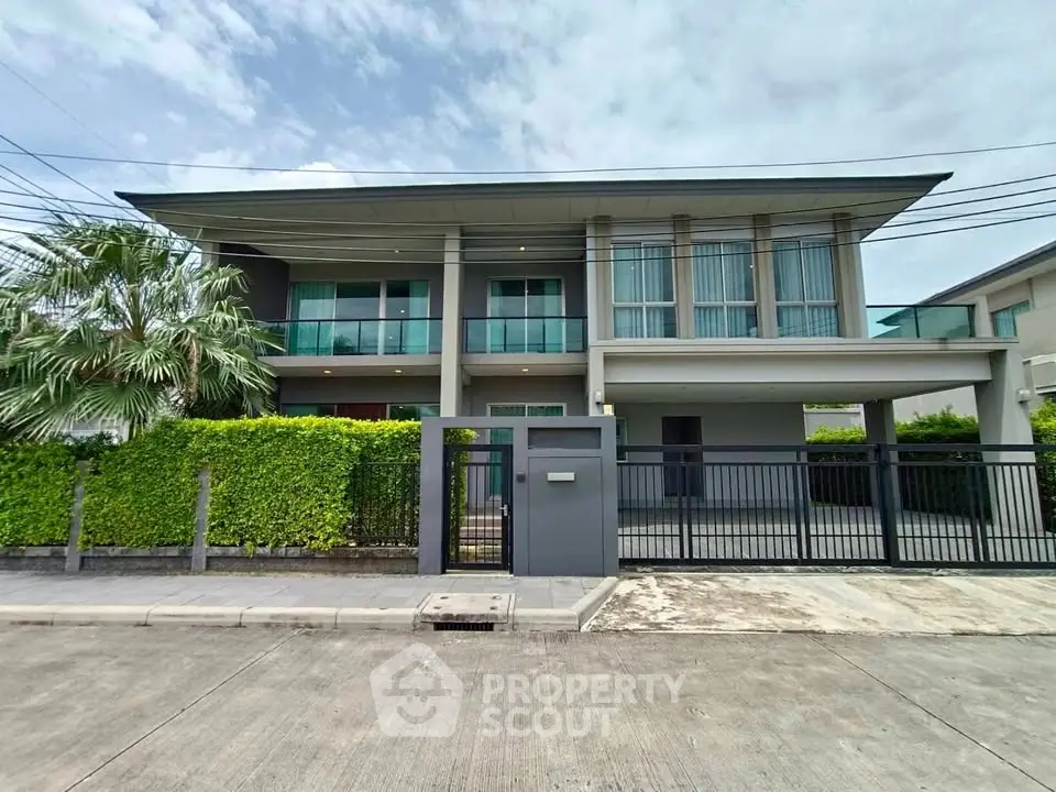 Modern two-story house with sleek design, large windows, and lush greenery in a suburban neighborhood.