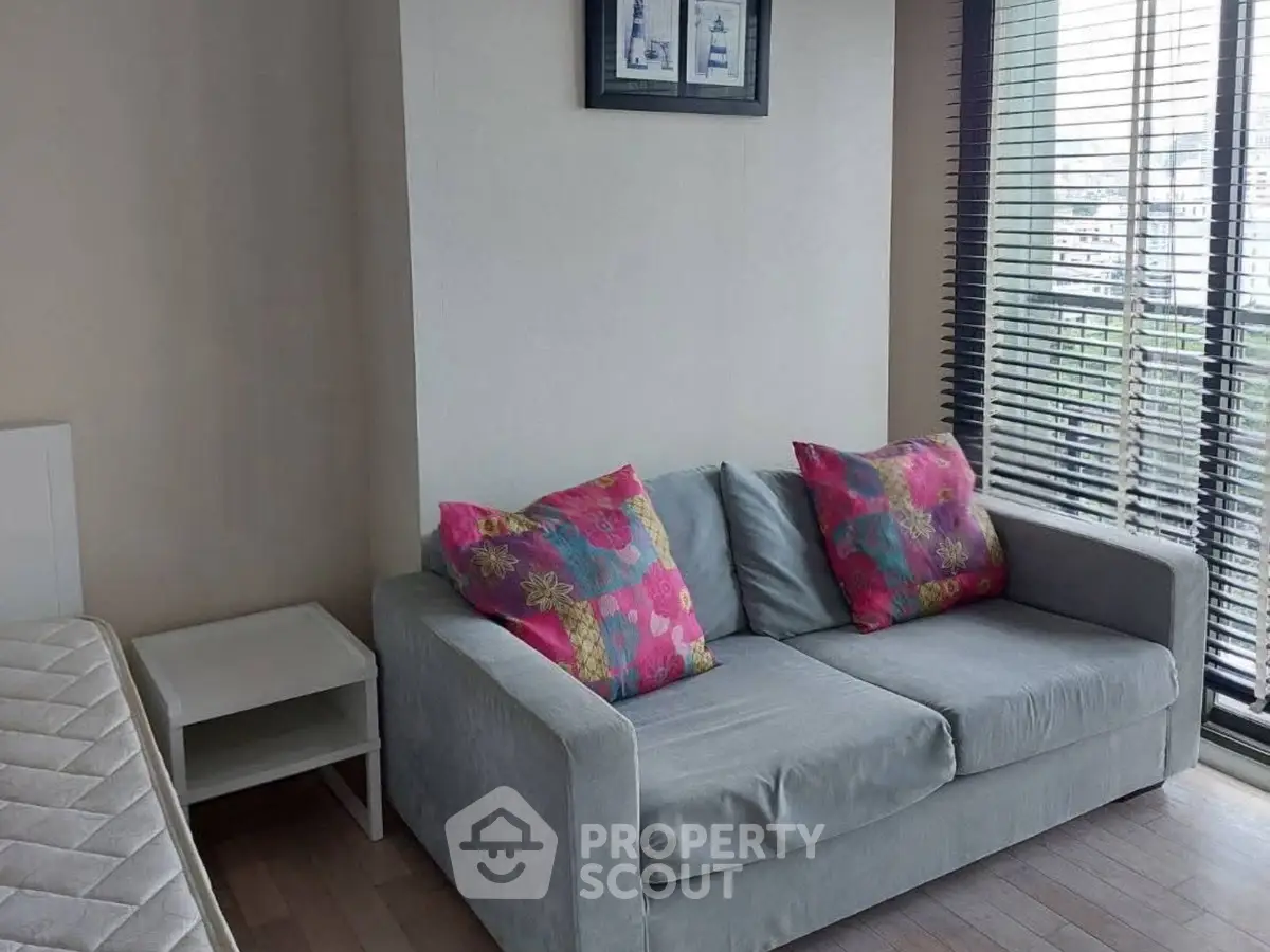 Cozy living room with sofa and vibrant cushions, featuring large windows with city view.