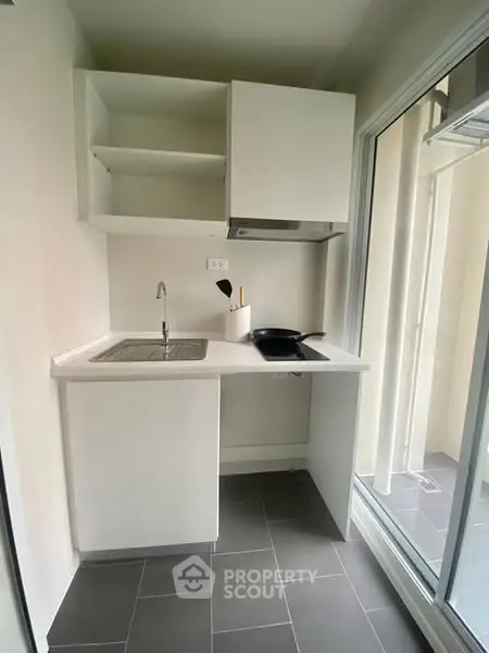 Compact modern kitchen with sleek white cabinets and large window for natural light.