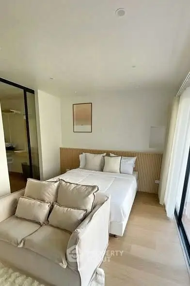 Modern bedroom with cozy sofa and stylish decor, featuring large windows for natural light.
