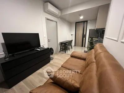 Modern living room with brown leather sofa, sleek TV setup, and compact kitchen area.