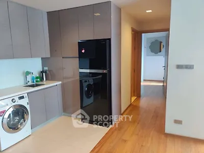 Modern kitchen with sleek cabinets, washing machine, and black fridge in a stylish apartment.