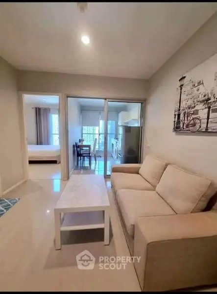 Modern living room with beige sofa and white coffee table, open layout to dining area and bedroom.