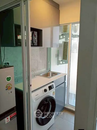 Modern compact kitchen with washing machine and sleek cabinetry in a bright apartment.