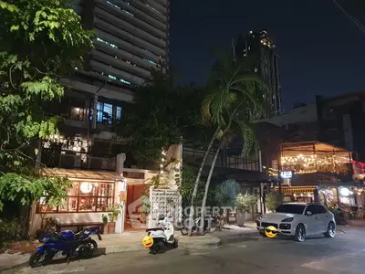 Charming urban street view with modern buildings and lush greenery at night.