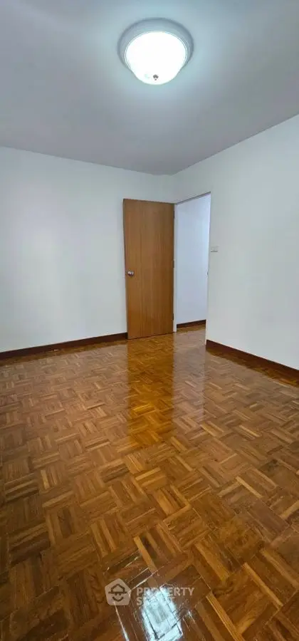 Spacious empty room with polished wooden flooring and white walls