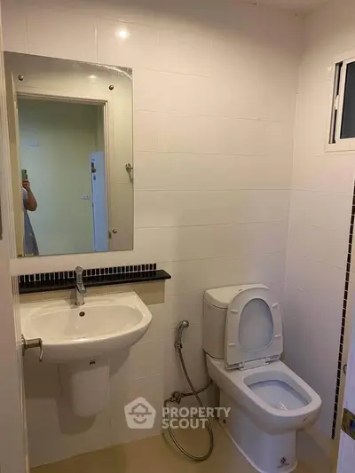 Modern bathroom with white tiles, sink, and toilet in a real estate property.