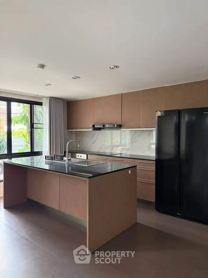 Modern kitchen with sleek cabinetry and large black refrigerator in a bright, airy space.