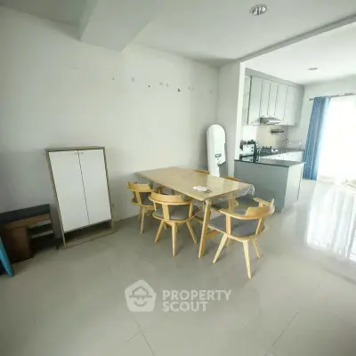 Modern dining area with sleek kitchen and natural light, featuring stylish wooden chairs and a minimalist design.