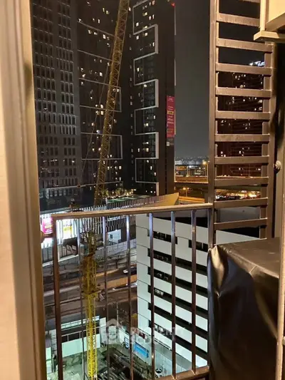 Urban balcony view with construction crane and city lights at night
