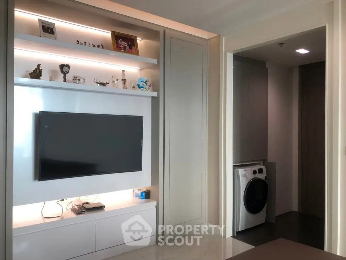 Modern living room with built-in TV unit and adjacent laundry area featuring a washing machine.