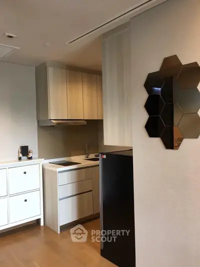Modern kitchen with sleek cabinetry and compact design, featuring a black fridge and stylish wall decor.