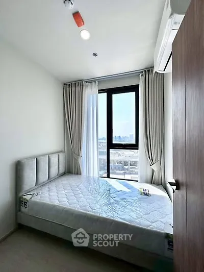 Bright bedroom with large window and modern furnishings in a high-rise apartment.