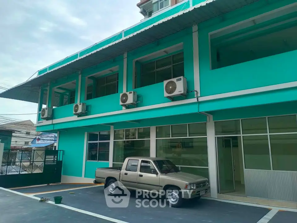 Modern turquoise building exterior with parking area and air conditioning units