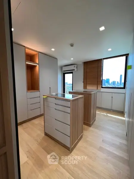 Spacious modern kitchen with island and city view, featuring sleek cabinetry and wooden flooring.