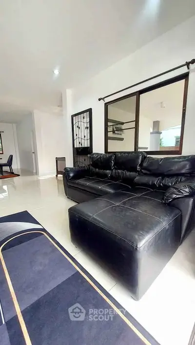 Spacious living room with modern black leather sofa and open layout design.