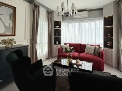 Elegant living room with red sofa, modern chandelier, and large windows for natural light.