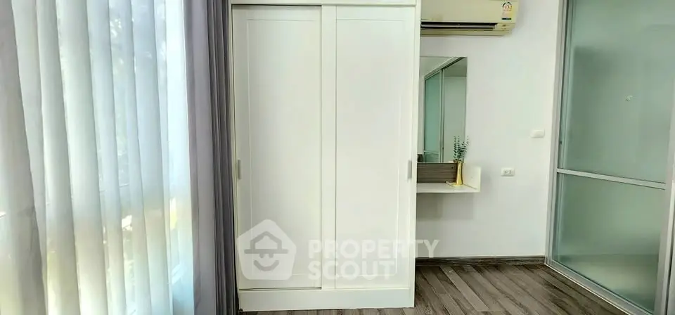 Modern bedroom with sleek wardrobe and air conditioning, featuring natural light and minimalist decor.