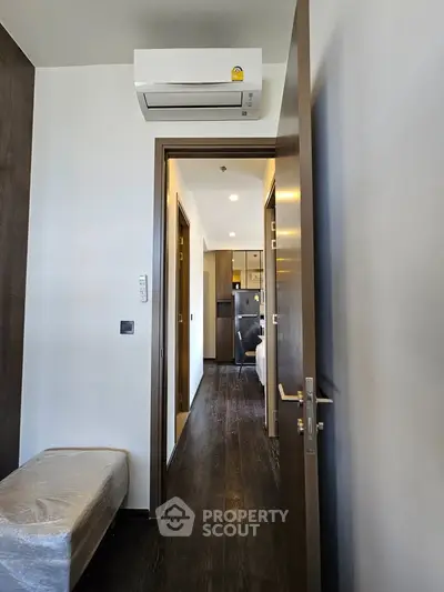 Modern apartment hallway with air conditioning and wooden flooring leading to a cozy bedroom.