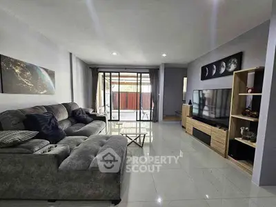 Spacious modern living room with plush sofa and large TV, leading to a bright balcony.