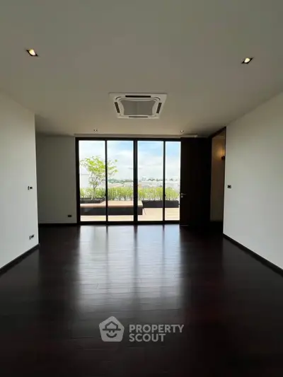 Spacious room with dark wood flooring and large windows opening to a balcony with a view.