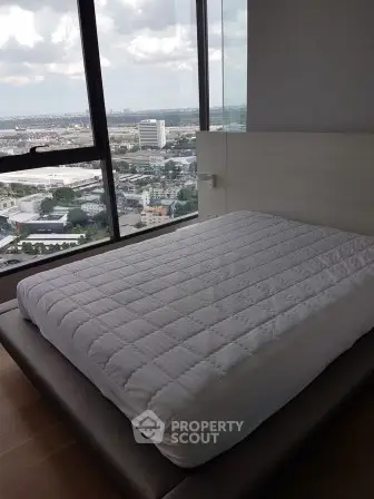 Modern bedroom with panoramic city view and large windows in high-rise apartment.
