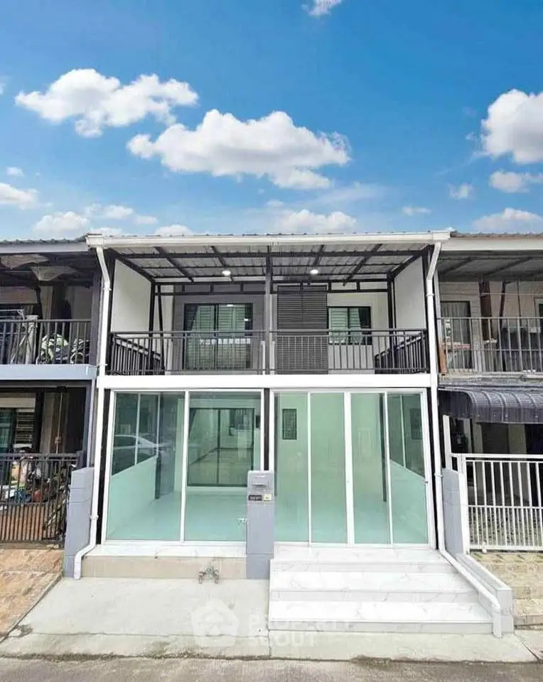 Modern two-story townhouse with glass facade and balcony under clear blue sky.