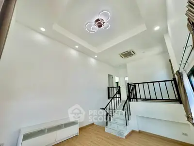 Modern living room with stylish ceiling light and staircase, featuring minimalist design and ample natural light.